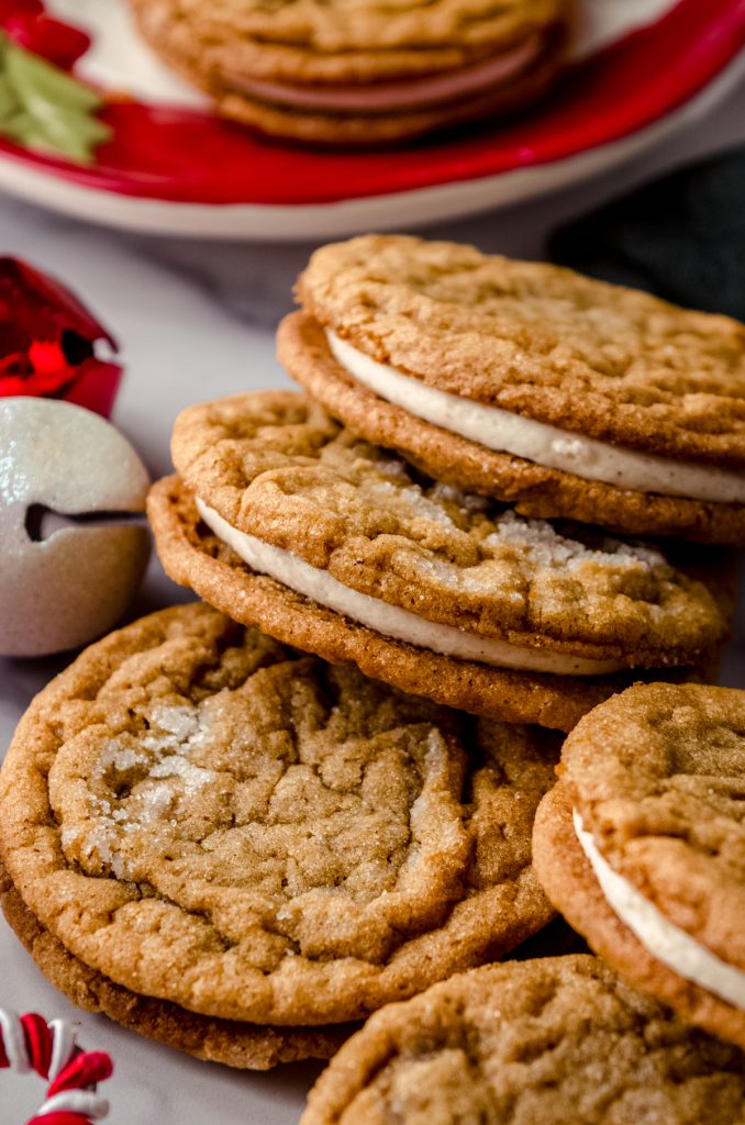 Gingerbread sandwich cookies on a surface and you can see Christmas bells and other decor in the background.