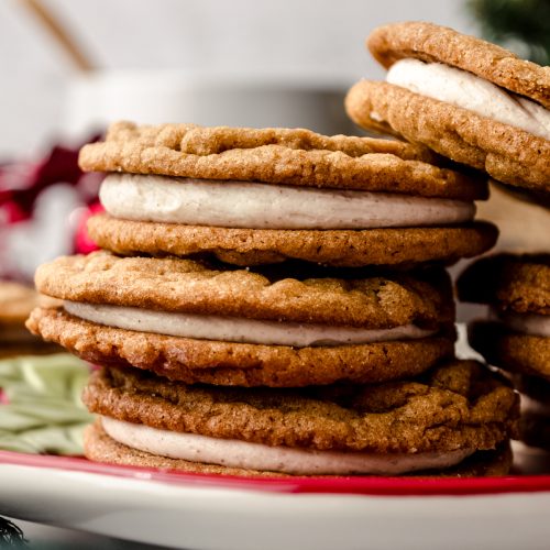 Gingerbread sandwich cookies sitting on a plate and you can see a mug and Christmas decor in the background.