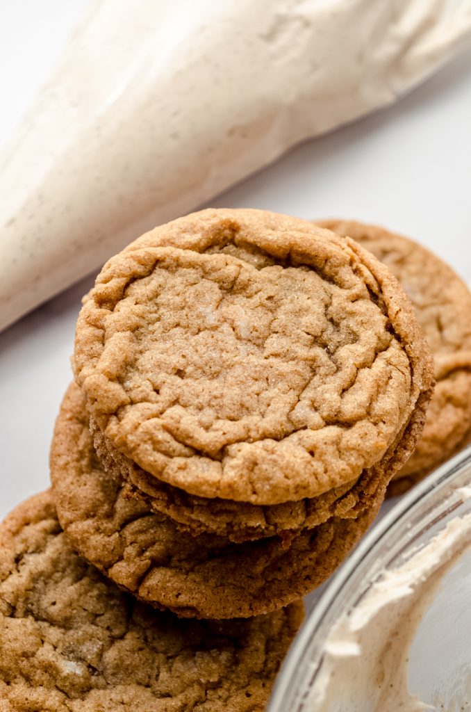 Gingersnap cookies on a surface and you can see a piping bag filled with cinnamon marshmallow frosting in the background.