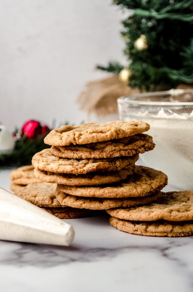 Gingersnap cookies on a surface with a Christmas tree and other Christmas decor in the far background.