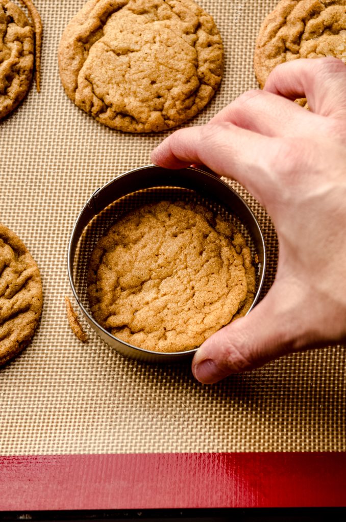 Someone is using a cookie cutter to reshape a hot gingersnap cookie.