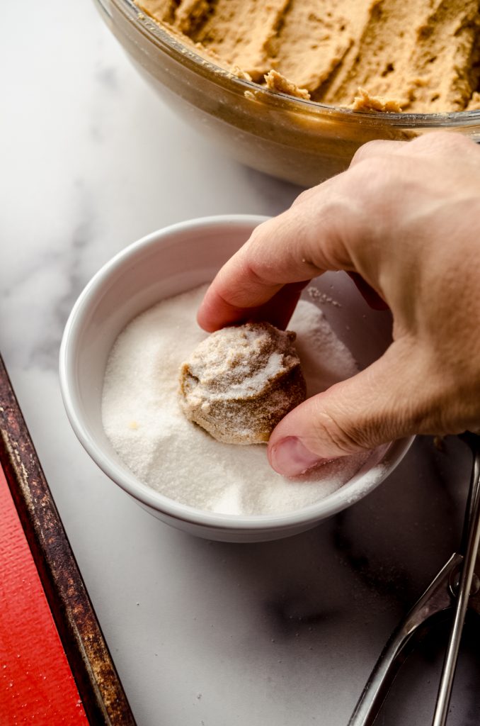 Someone is using their fingers to roll a ball of gingerbread cookie dough in sugar.