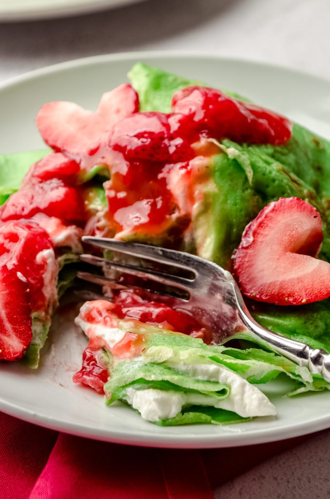 Grinch crepes on a plate with a fork and strawberries cut into heart shapes.