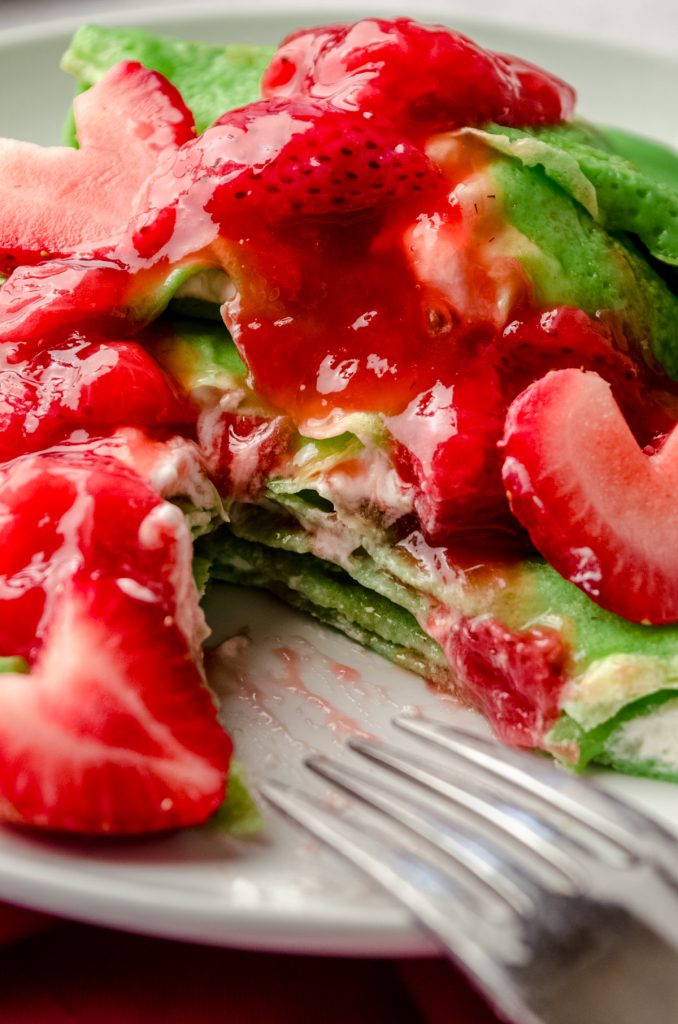 Grinch crepes on a plate with a fork and strawberries cut into heart shapes.