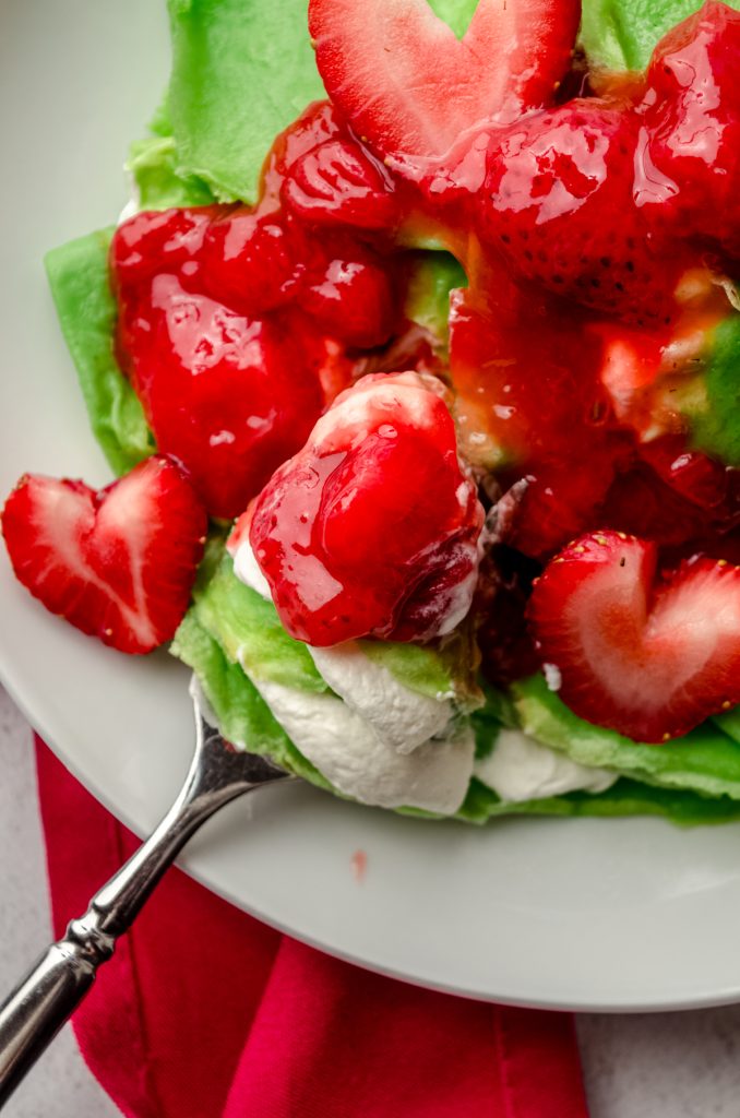 Grinch crepes on a plate with a fork and strawberries cut into heart shapes.