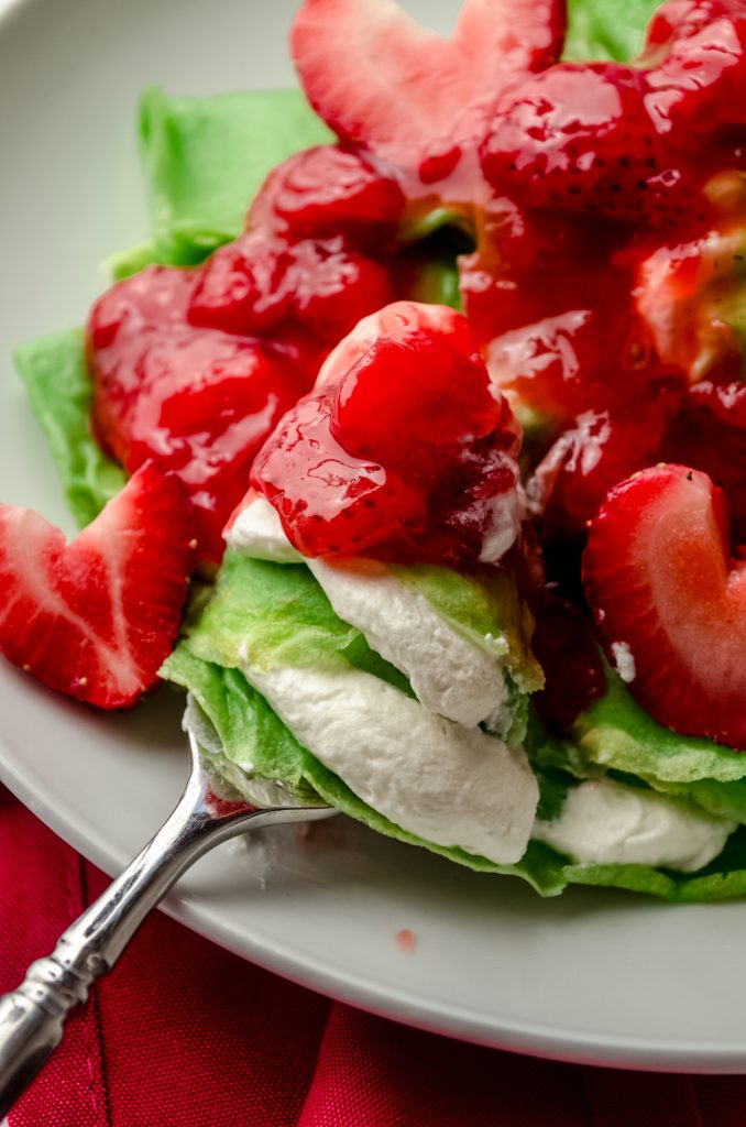 Grinch crepes on a plate with a fork and strawberries cut into heart shapes.