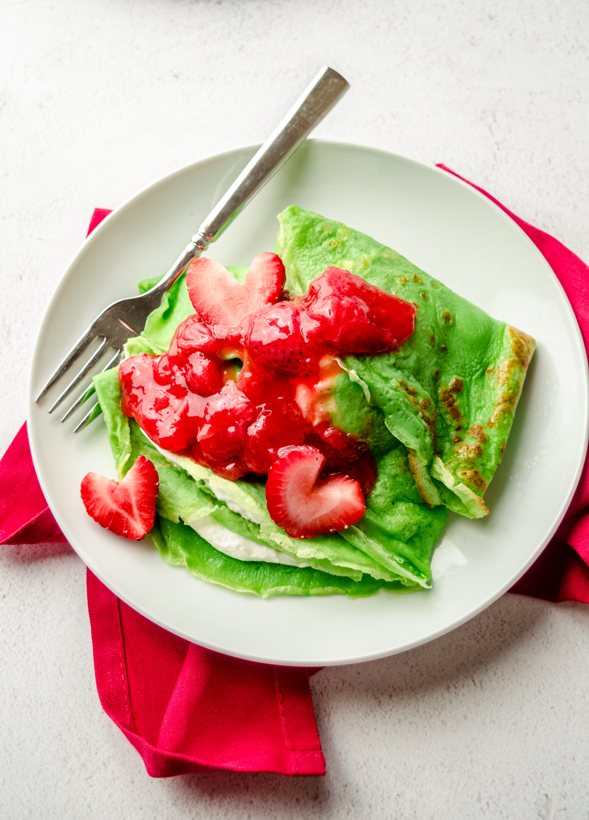 Aerial photo of Grinch crepes on a plate with a fork and strawberries cut into heart shapes.