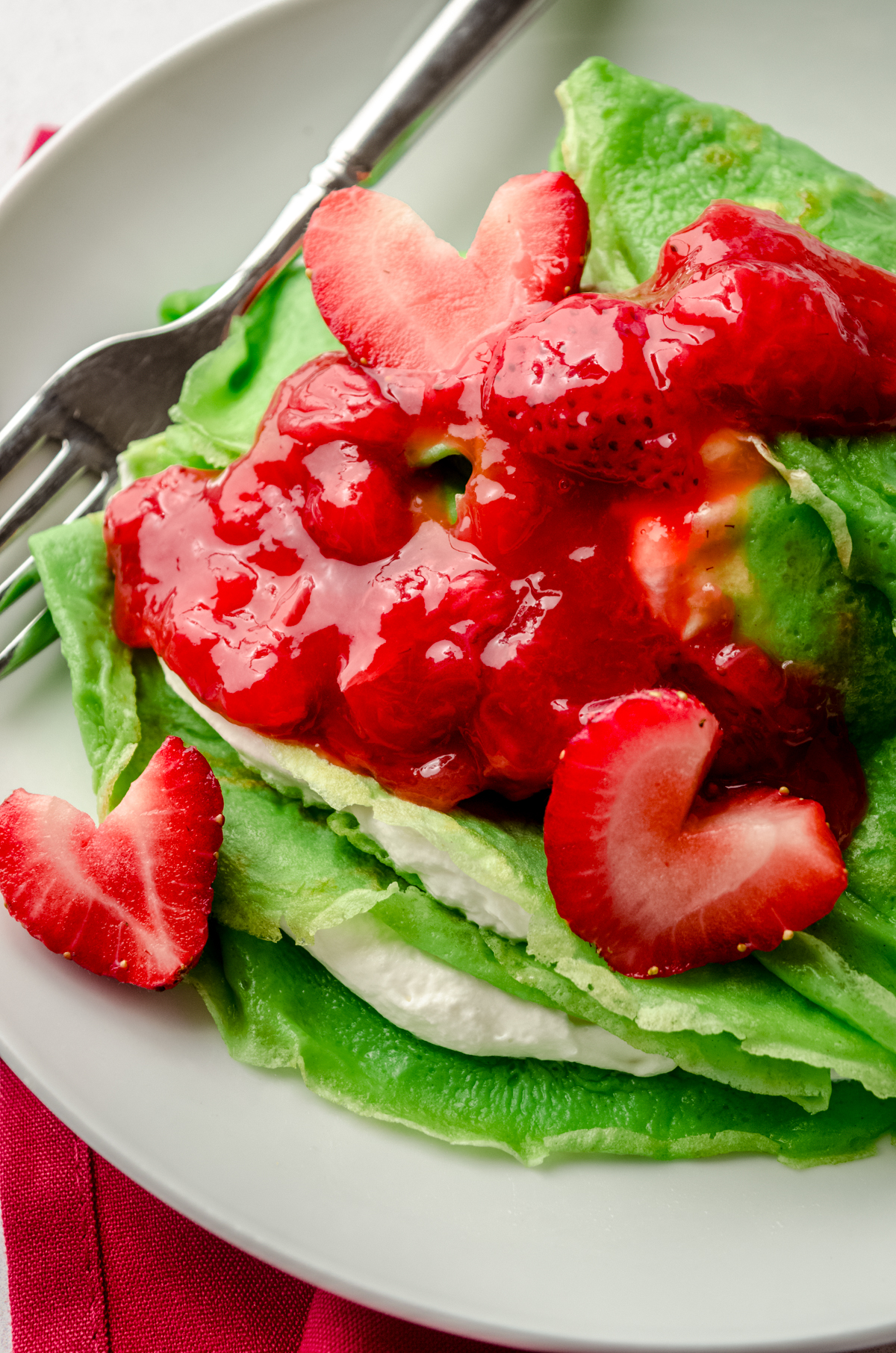 Grinch crepes on a plate with a fork and strawberries cut into heart shapes.