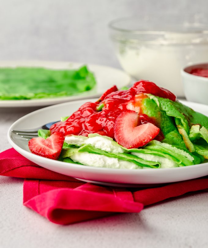 Grinch crepes on a plate with a fork and strawberries cut into heart shapes.