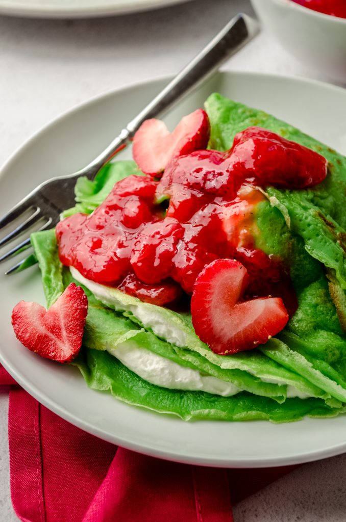 Grinch crepes on a plate with a fork and strawberries cut into heart shapes.