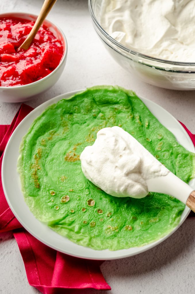 Someone is filling a green crepe with fresh whipped cream.