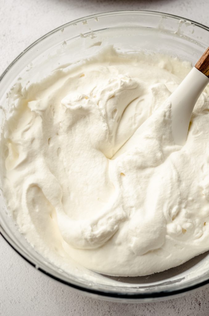 A large bowl of whipped cream with a spatula in it.