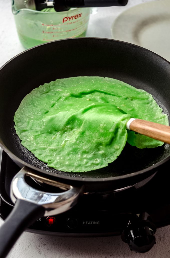 Someone is using a large spatula to flip a green crepe to make Grinch crepes.