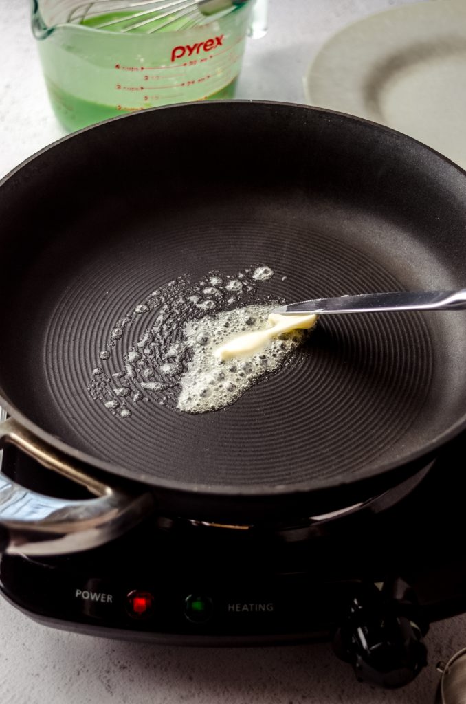 Someone is buttering a pan with a butter knife preparing it to make crepes.