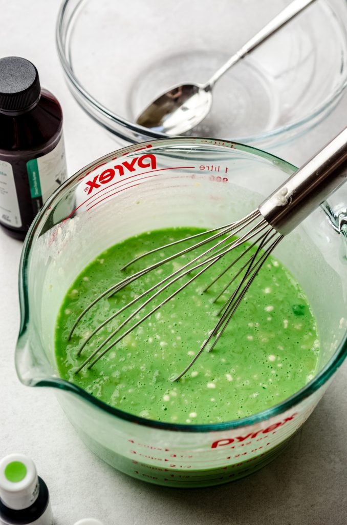 Green crepe batter in a large measuring cup with a whisk.