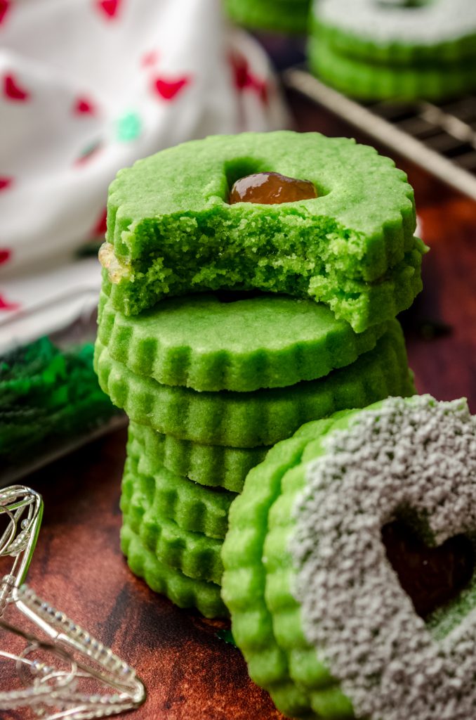 A stack of Grinch Linzer cookies on a surface and a bite has been taken out of the one on the top.