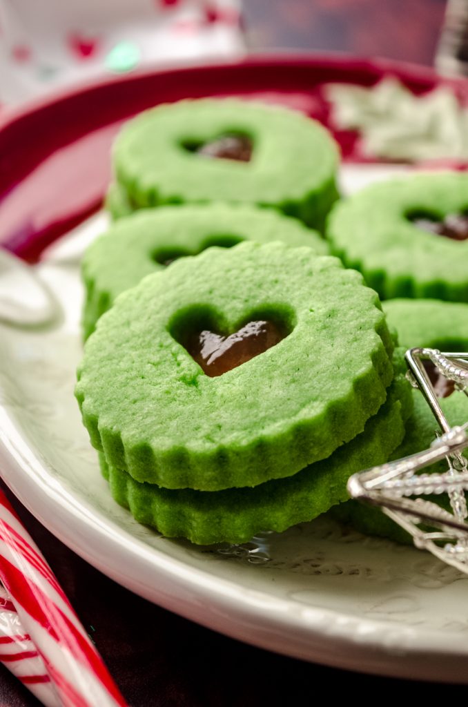 Grinch Linzer cookies on a plate with Christmas decor around it.