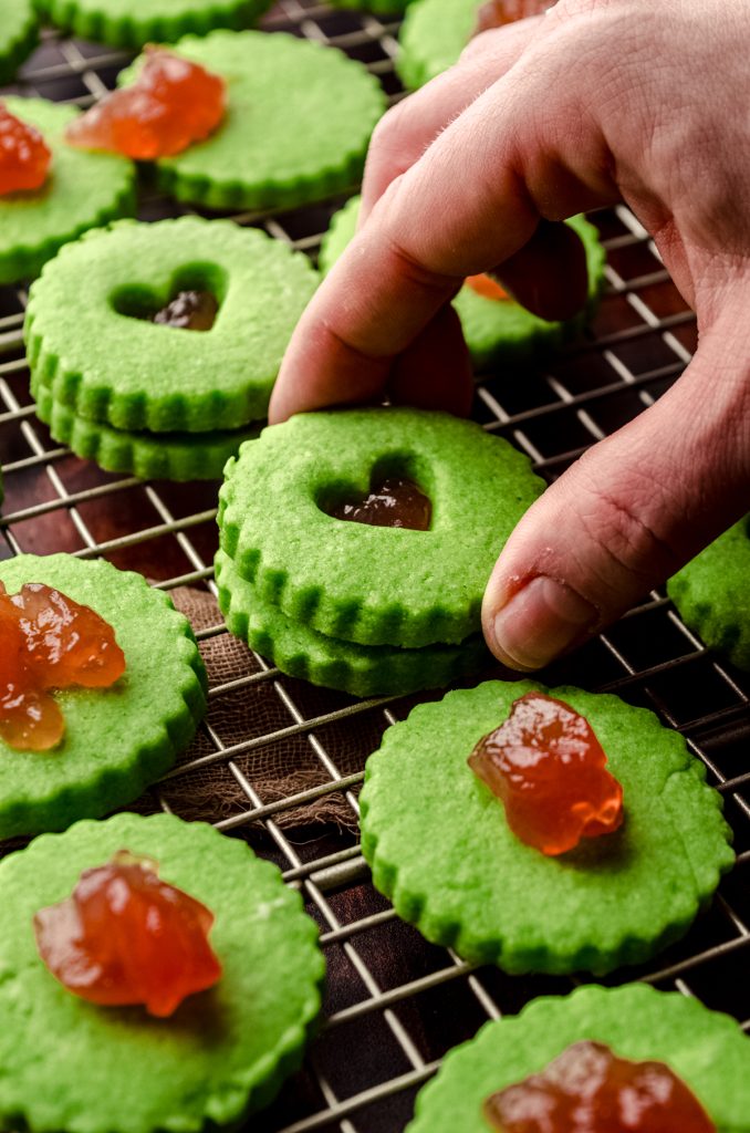 Someone is placing the top cookie on a Grinch Linzer sandwich cookie.