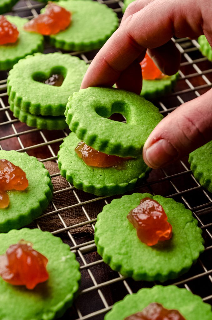 Someone is placing the top cookie on a Grinch Linzer sandwich cookie.