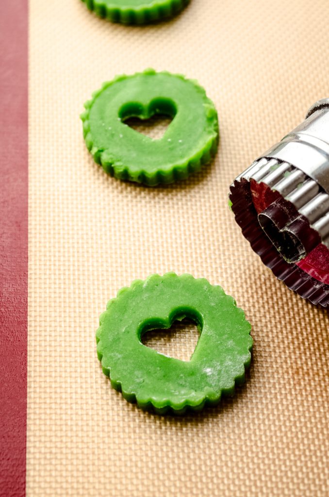 Grinch Linzer cookies on a baking sheet with a Linzer cookie cutter on a baking sheet.