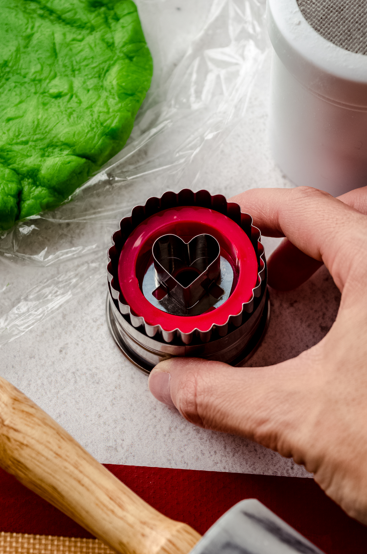 Someone's hand holding a Linzer cookie cutter in a cookie rolling workspace.