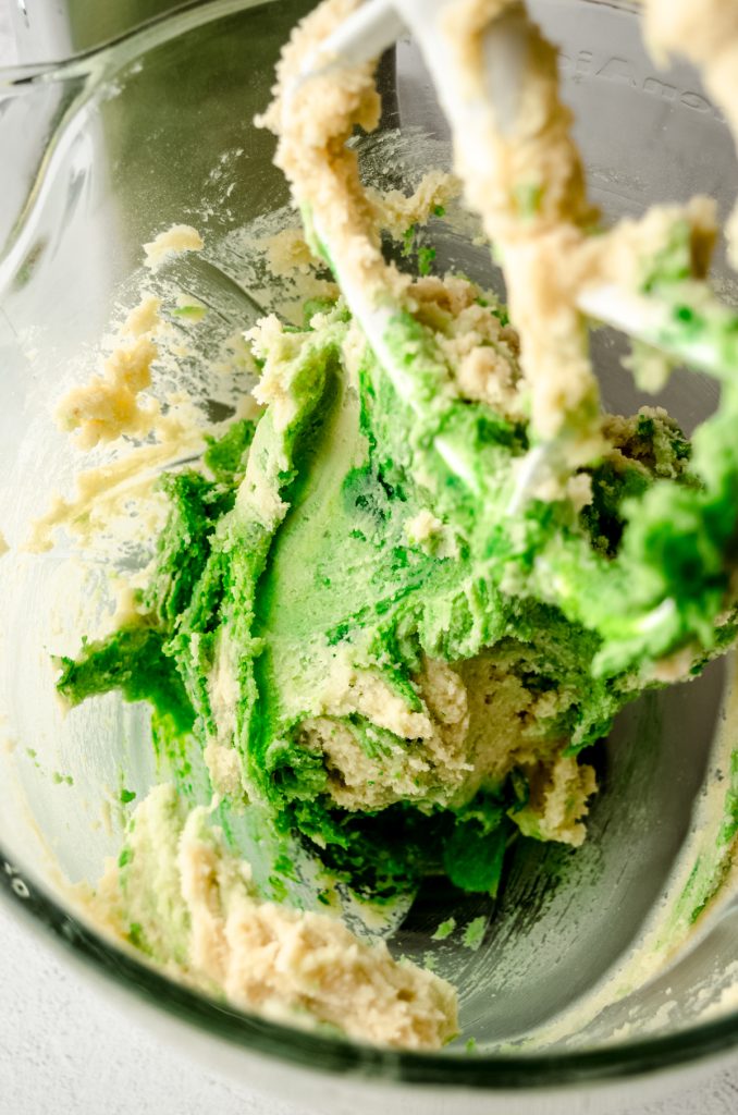 Green Linzer cookie dough in the bowl of a mixer fitted with the paddle attachment.