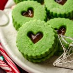 Grinch Linzer cookies on a plate with Christmas decor around it.