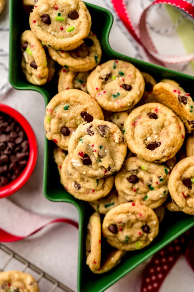 Aerial photo of mini Christmas chocolate chip cookies with festive sprinkles in it sitting in a tree shaped bowl.