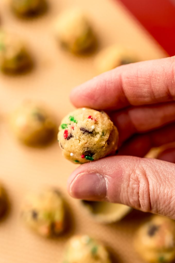 Someone's hand holding a ball of Christmas chocolate chip cookie dough.