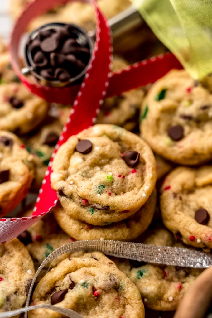 Mini Christmas chocolate chip cookies on a surface with festive ribbon and chocolate chips around them.