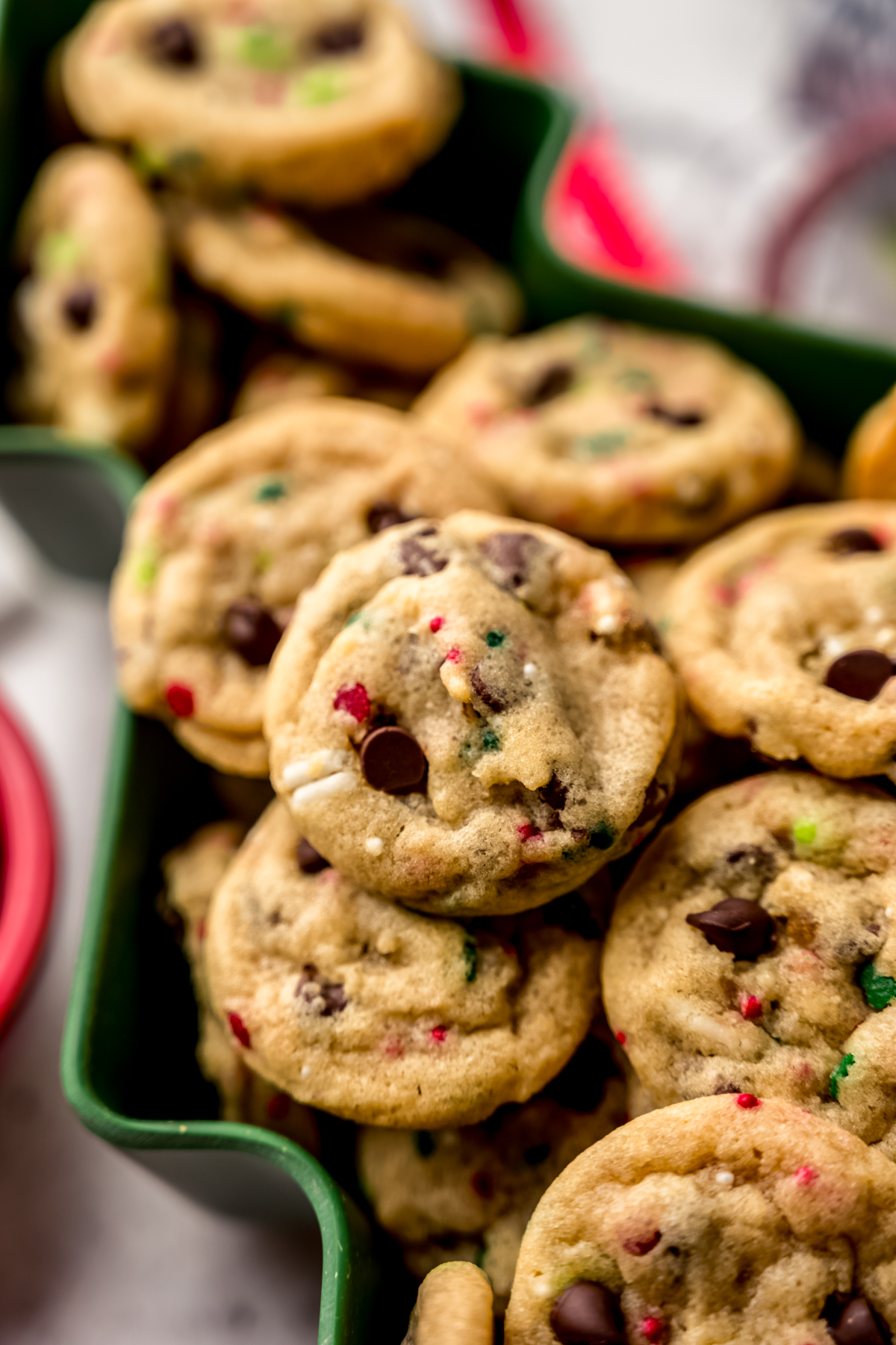 Mini Christmas chocolate chip cookies with festive sprinkles in it sitting in a tree shaped bowl.