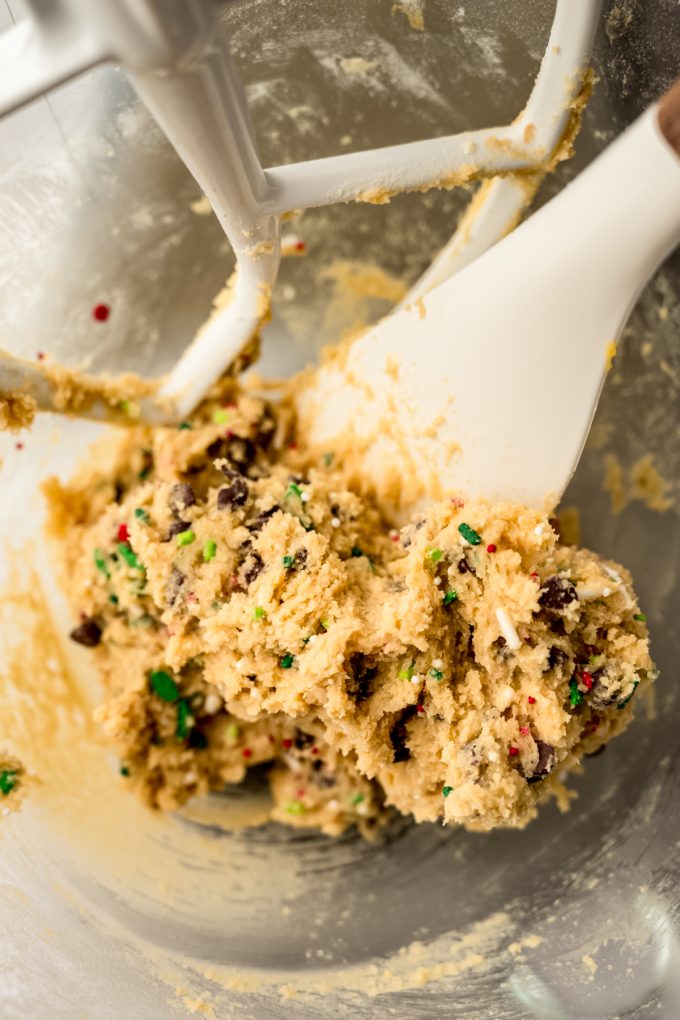 Christmas chocolate chip cookie dough in the bowl of a stand mixer with a spatula in it.