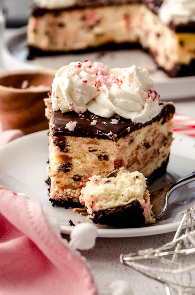 A slice of peppermint bark cheesecake on a plate with a fork and a bite taken out of the slice.