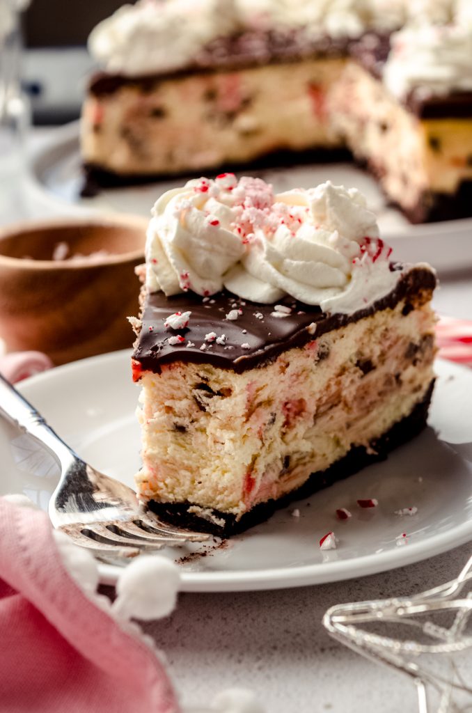 A slice of peppermint bark cheesecake on a plate with a fork and a bite taken out of the slice.