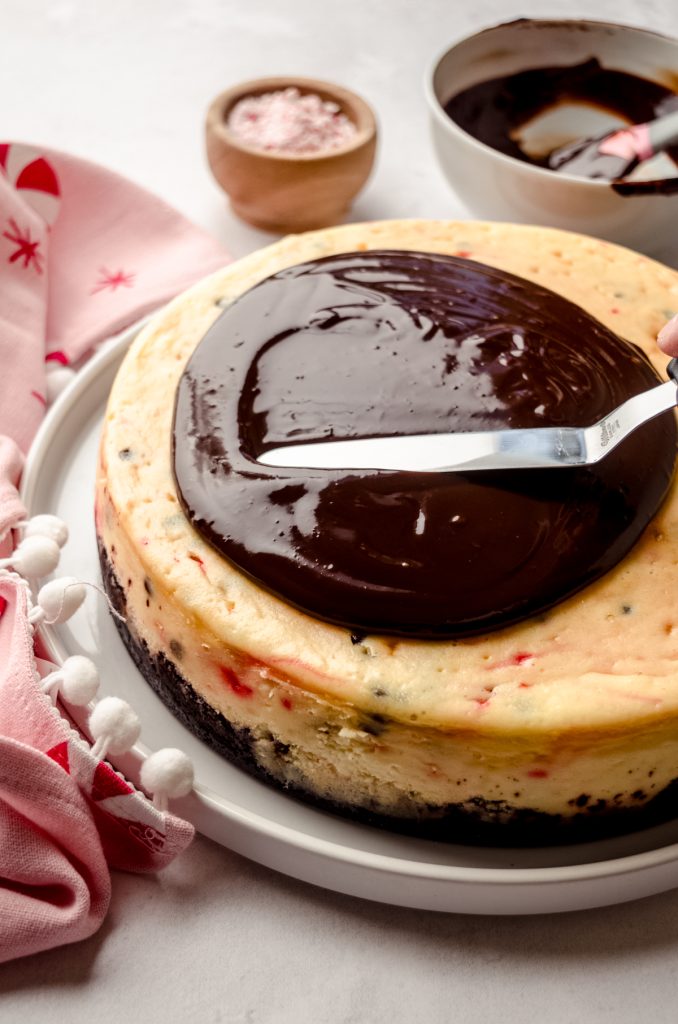 Someone is spreading ganache onto a peppermint bark cheesecake.