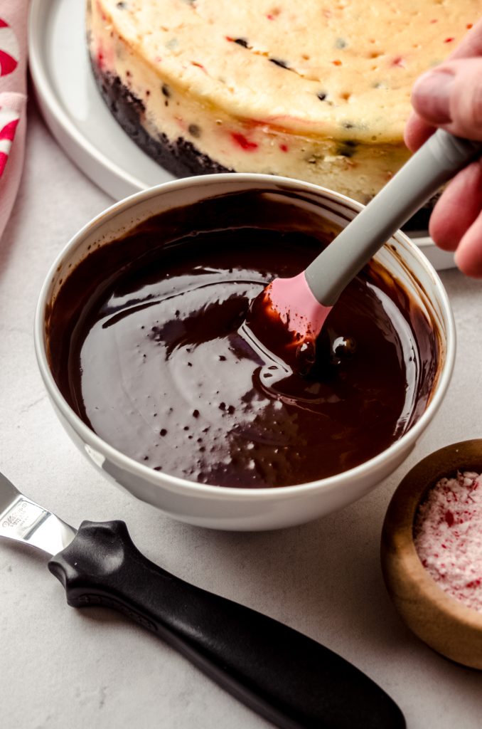 Someone is stirring a bowl of chocolate ganache with a pink and gray spatula.