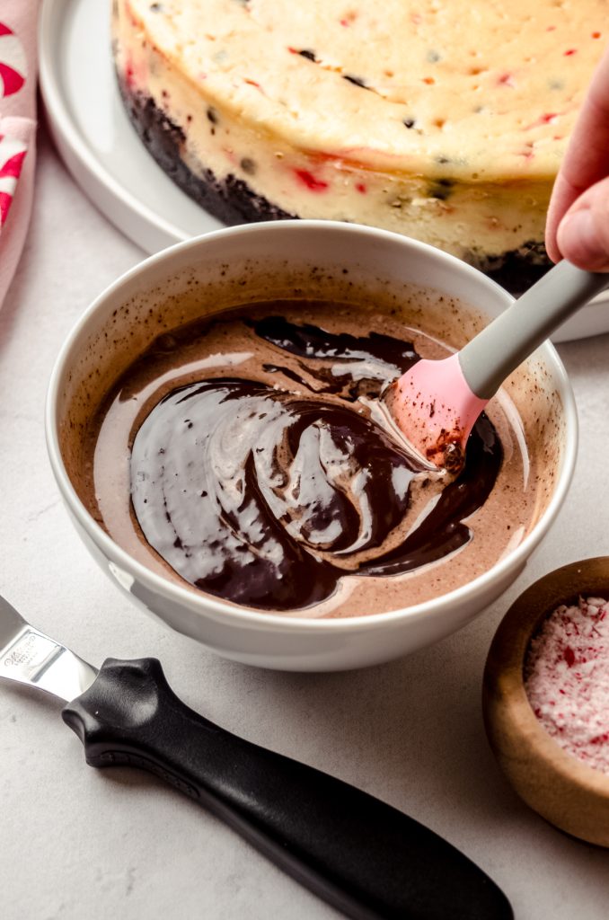 Someone is stirring a bowl of chocolate ganache with a pink and gray spatula.