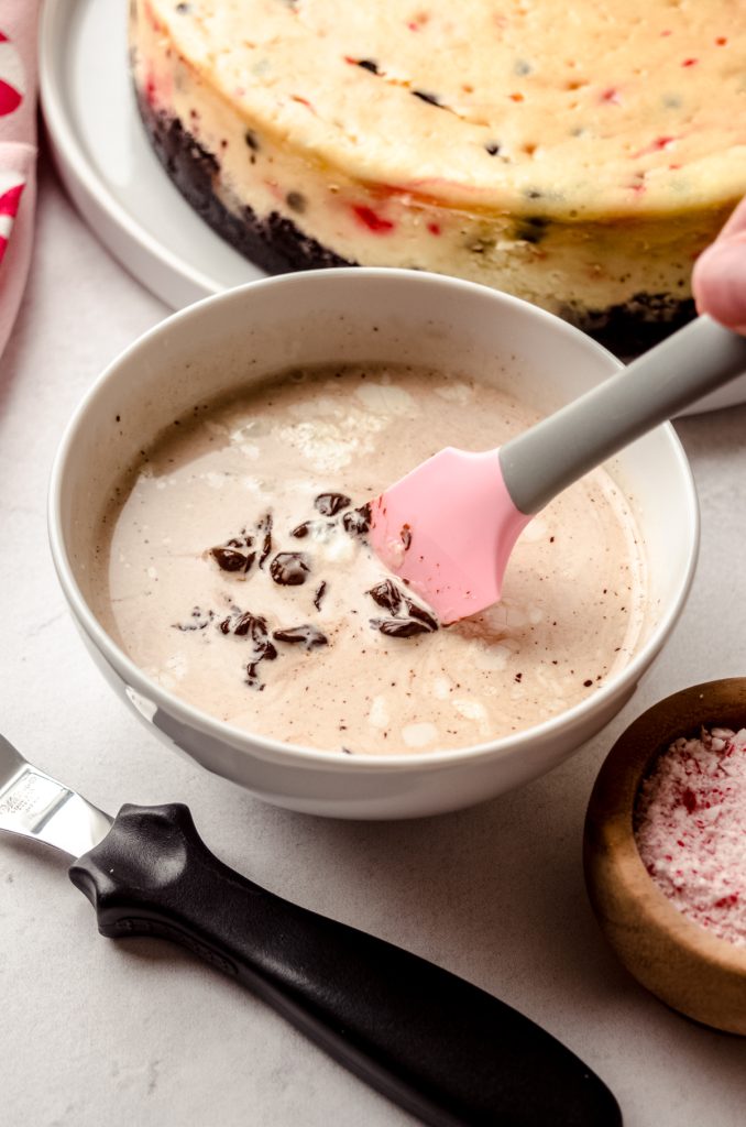 Someone is stirring a bowl of chocolate ganache with a pink and gray spatula.