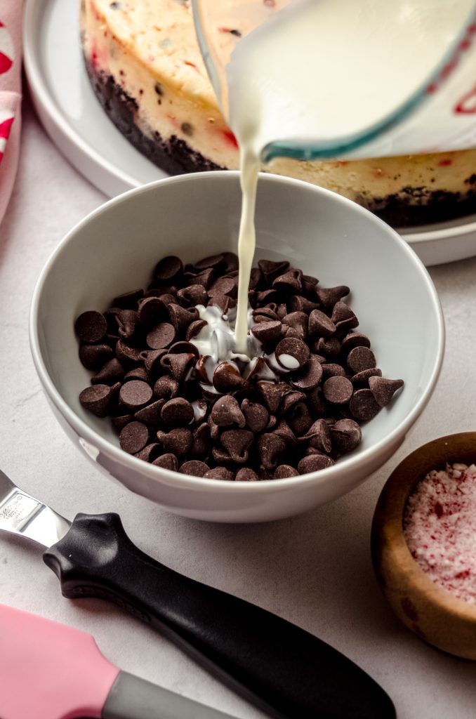 Someone is pouring warm heavy cream over chocolate chunks to make chocolate ganache.