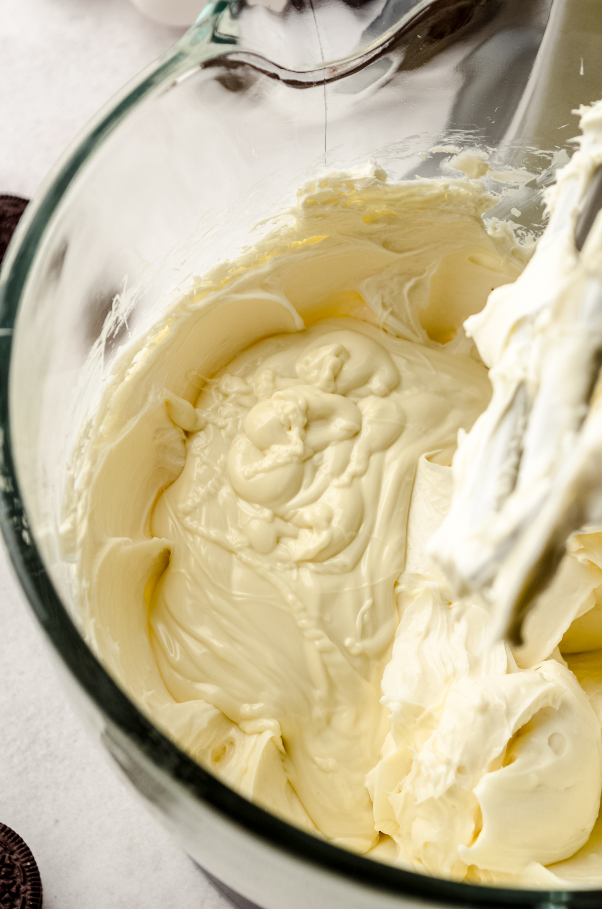 Cheesecake batter in the bowl of a mixer that has just had melted and cooled white chocolate mixture poured into it.