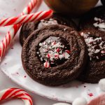 Chocolate peppermint thumbprint cookies on a plate with candy canes around it.