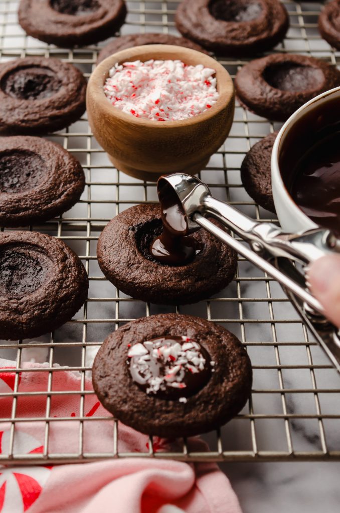 Someone is using a mini cookie scoop to fill a chocolate peppermint thumbprint cookie.