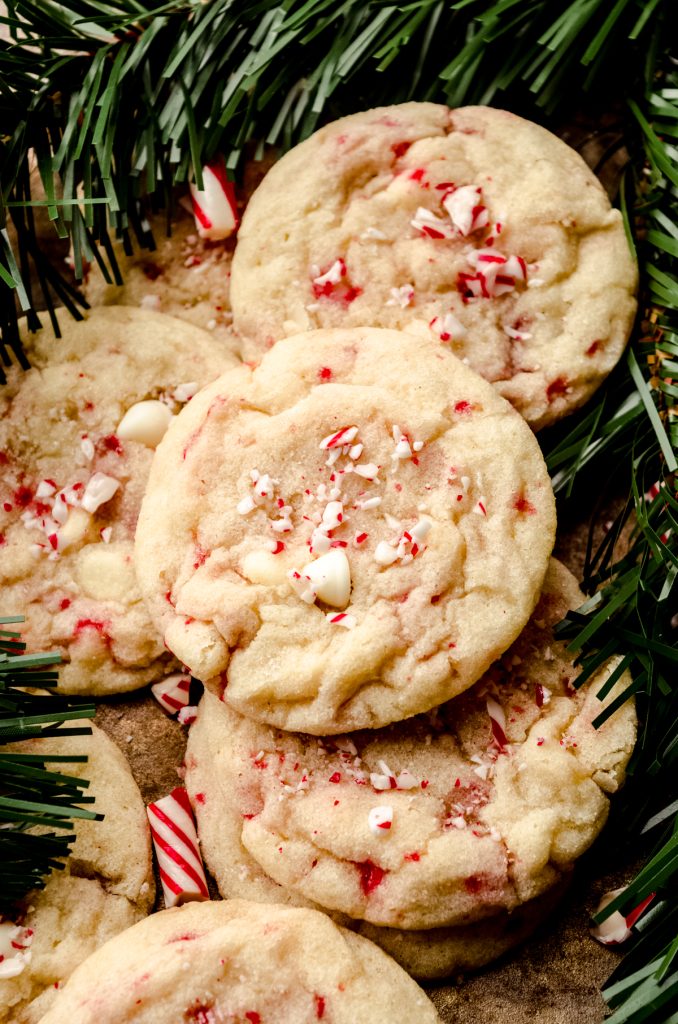 White chocolate chip peppermint cookies on a surface with candy cane pieces and evergreen needles around it.