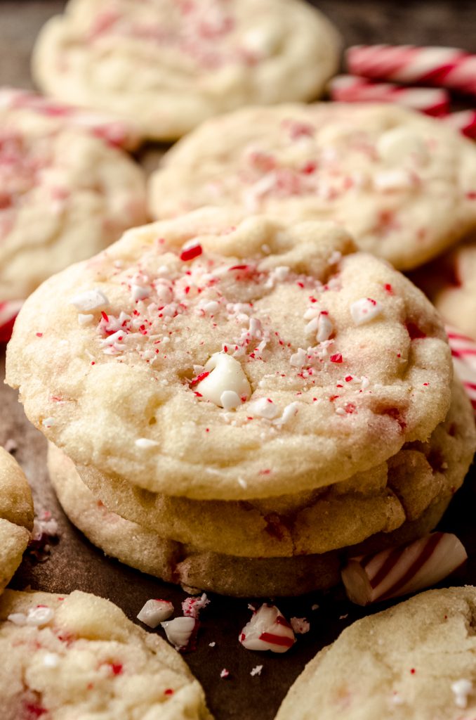 A stack of white chocolate chip peppermint cookies on a surface with candy cane pieces around it.