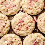 White chocolate chip peppermint cookies on a surface with candy cane pieces around it.