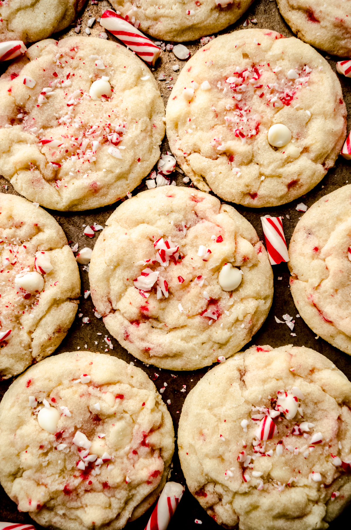 White chocolate chip peppermint cookies on a surface with candy cane pieces around it.