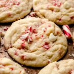 A white chocolate chip peppermint cookie on a surface with candy cane pieces around it.