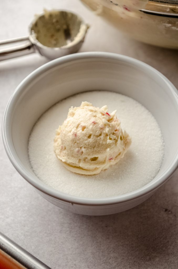 A ball of white chocolate peppermint cookie dough in a bowl of sugar.