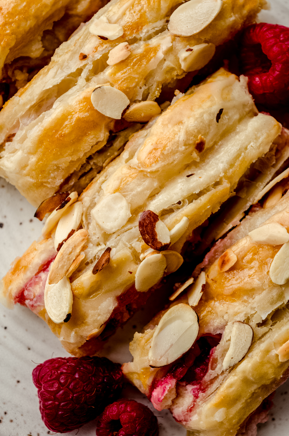 A pastry braid filled with raspberries and cream cheese with toasted almonds and an icing on it sliced into portions.