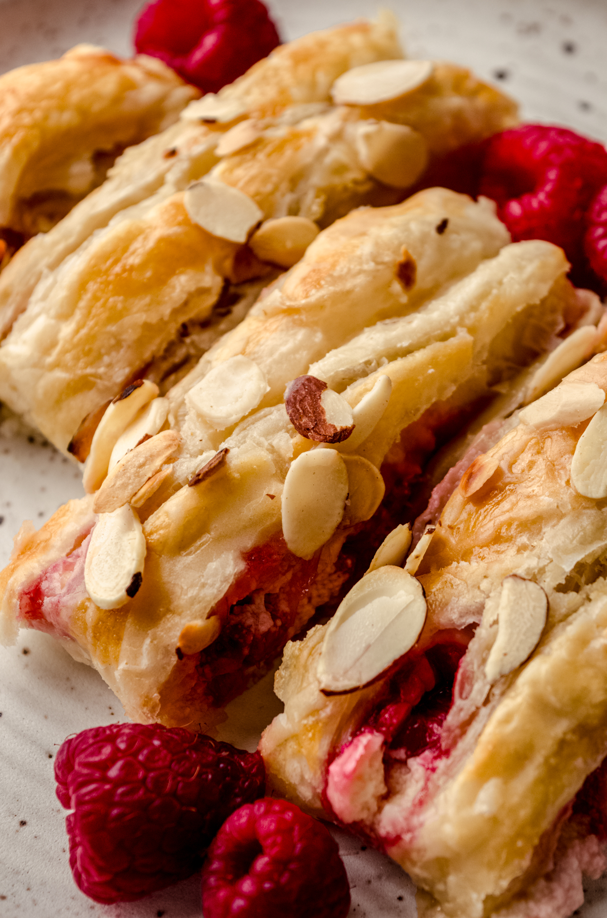 A pastry braid filled with raspberries and cream cheese with toasted almonds and an icing on it sliced into portions.